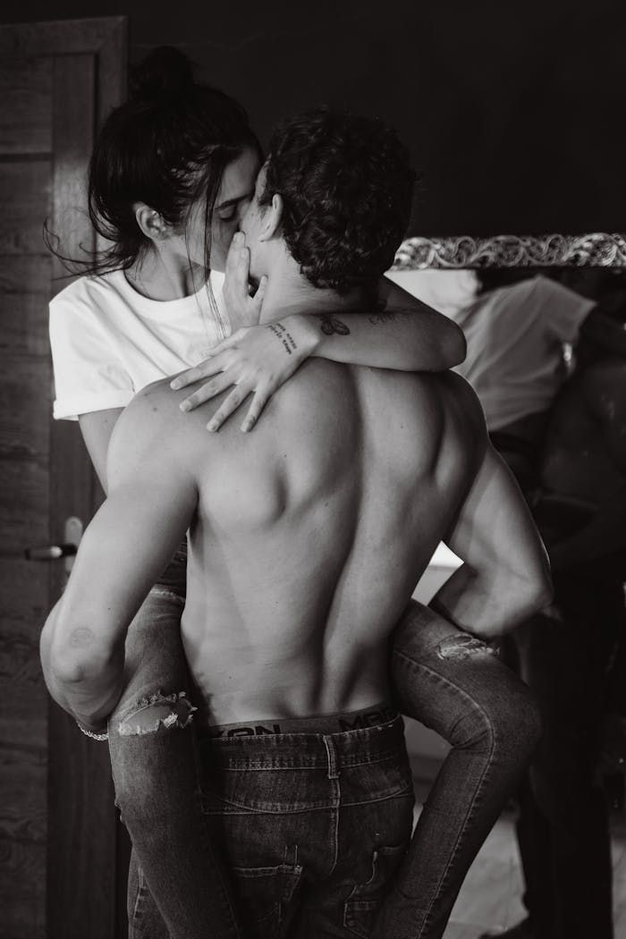 A couple shares a passionate kiss indoors, captured in a black and white photograph.